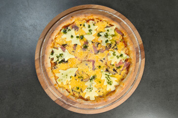 Top view of New year style pizza with ham, Gouda cheese served on wooden board. Kids food. Pizza decorated with holiday Christmas cheese trees. Served with pesto sauce. Dark stone background.
