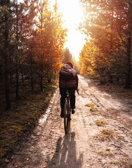 Young guy in a helmet rides a bicycle on a trail in the autumn forest.
