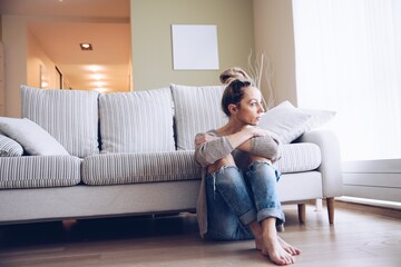 A lonely young woman feels depressed and stressed. She is sitting on the floor. Concept of negative...