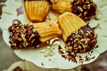 Close up of madeleines dipped in chocolate and chopped nuts served on fancy metal cutwork dessert plate.
