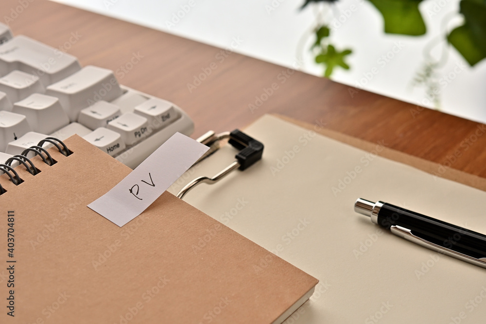 Poster a sticky note labeled pv is taped to the edge of a notebook on the desk.that's an acronym for page v