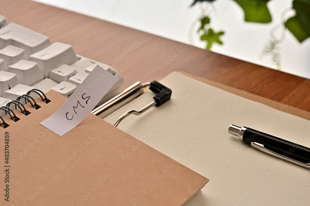 Poster a sticky note labeled cms is taped to the edge of a notebook on the desk.that's an acronym for conte