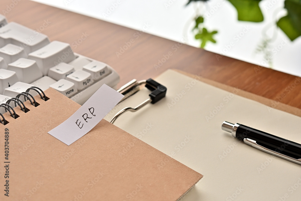Poster a sticky note labeled erp is taped to the edge of a notebook on the desk.that's an acronym for enter
