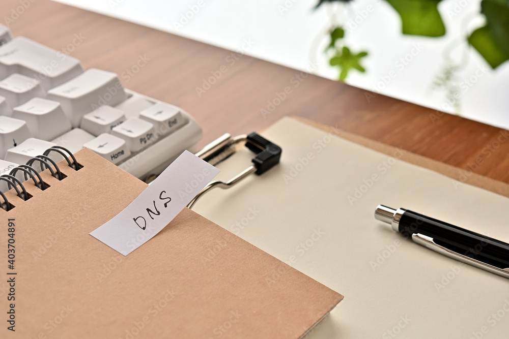 Poster a sticky note labeled dns is taped to the edge of a notebook on the desk.that's an acronym for domai