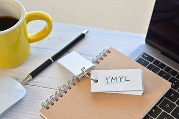 There's a word book on a desk cluttered with papers. The word YMYL is written in it. It's an abbreviation for Your Money or Your Life.