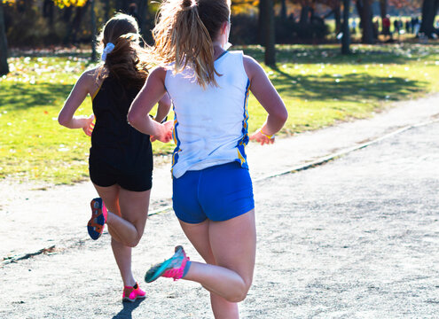 Two high school girls running in a cross country race on a gravel path