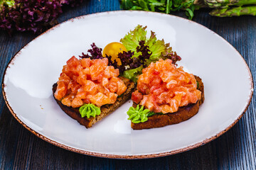 Healthy toasts with rye bread with salmon, avocado mousse, lettuce on white plate.