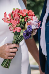 Closeup portrait of bride holding a beautiful colorful wedding bouquet standing next to groom