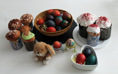 Soft toy Easter bunny, painted eggs in a wooden bowl and Easter cakes on a white table. The concept of gifts and decorations of the Bright Easter holiday