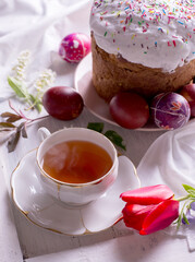 Happy Easter breakfast still life with White porcelain cup of tea, colored eggs, and Easter cake.