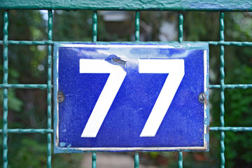 A blue house number plaque, showing the number seventy seven (77)
