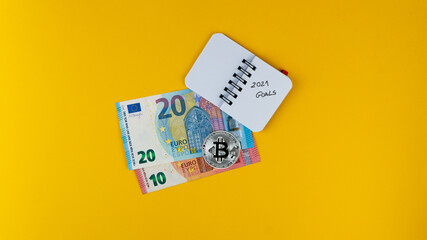 Overheadshot of Revolut credit card, euro banknotes,bitcoin and a small notebook with 