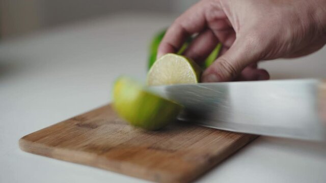Chico Latino corta un limon en una tabla de madera en la cocina. 