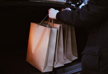 a young man puts paper shopping bags in the trunk of a car
