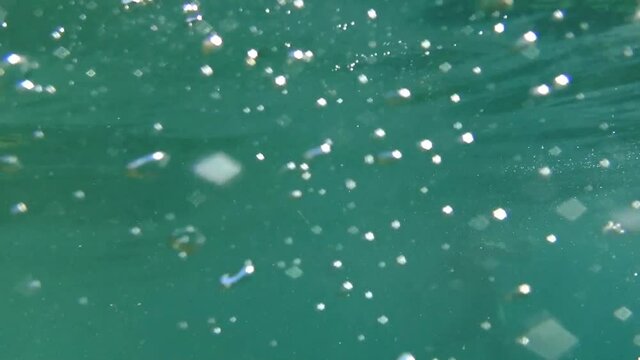 Underwater shot of children diving with air bubbles and waves under the water&rsquo;s surface.