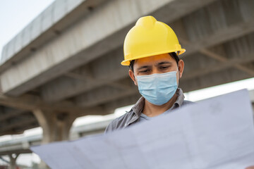 Asian construction workers wear masks and holding blueprints at construction sites.	
