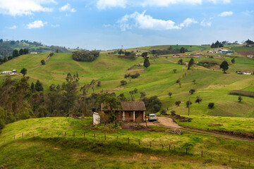 Obraz premium Small house with tiles with a car parked to one side in the middle of a country landscape between hills. Boyacá. Colombia.