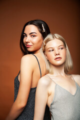 two pretty diverse girls happy posing together: blond and brunette on brown background, lifestyle people concept