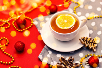 Christmas gingerbread cookies and a cup of tea with lemon, on a red background at home with shiny decorations and lights for New Year mood.