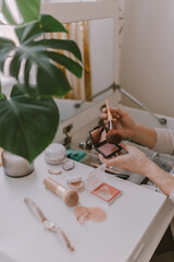 Everyday beauty routine. Make up artist. Dressing vanity. Women's hands. Pastel colors. In front of the mirror. Palettes, brushes, mascara, lipstick. White bright bedroom. Early morning light.