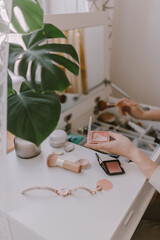 Everyday beauty routine. Make up artist. Dressing vanity. Women's hands. Pastel colors. In front of the mirror. Palettes, brushes, mascara, lipstick. White bright bedroom. Early morning light.