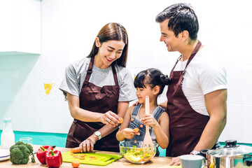 Happy family father and mother with daughter cooking and preparing meal together in the kitchen