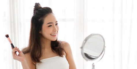 Smiling of young beautiful pretty woman clean fresh healthy white skin looking at camara.girl holding make-up brushes and make up on face with cosmetics set at home.facial beauty and cosmetic concept