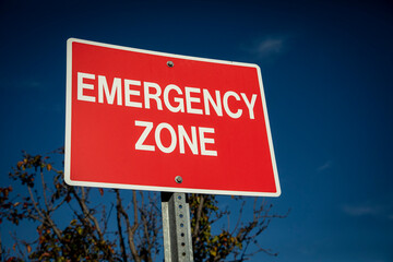 Red sign with white letters stating Emergency Zone against a blue sky