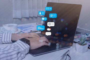 Person using a social media marketing concept on laptop with notification icons of like, chat, message and comment above laptop screen.