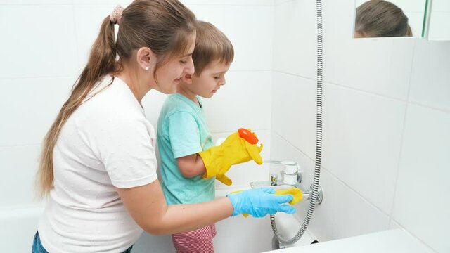 Smiling boy with mother washing bath and water sink. Children helping adults in housework and home cleanup.