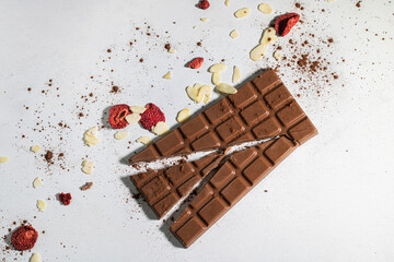 Broken bar of milk chocolate. Freeze-dried strawberries and almond flakes. Chocolate sprinkled with cocoa.