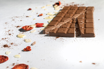 A bright background with a milk chocolate bar, freeze-dried strawberries and almond flakes. Dried fruits, cocoa. Food improving concentration.