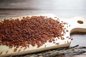 Red rice pile on wooden cutting board and ears of rice on wooden table.