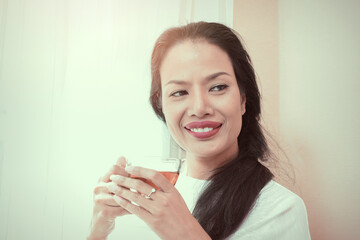 Beautiful black hair woman with red lips in white lace shirt standing by the window.