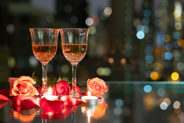 glass red wine, roses, petals and candles on table with reflection, twinkling blurred city night...