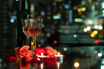 glass red wine, roses, petals and candles on table with reflection, twinkling blurred city night lights in background, romantic concept for lovers and valentine