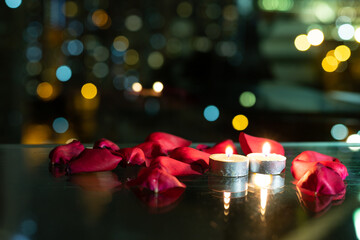 rose petals and candles on table with reflection, twinkling blurred city night lights in...