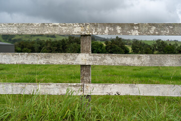 White farm fence made from wood with green fields in the background