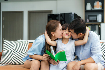 Happy Asian family with Father and Mother kiss in their daughter cheek together while sitting in living room at home. Love emotion, Smiling face, Enjoying, Joyful..