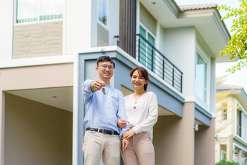 Portrait of Asian young couple standing and hugging together and holding house key looking happy in...