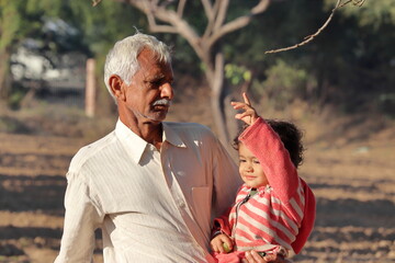 A beautiful Indian little child is cropped by hand and the Indian grandfather is seen cropping in the garden