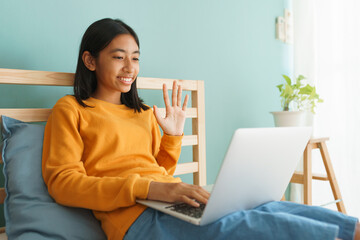 Happy Asian girl waving in greeting online tutor on  laptop computer in the interior home