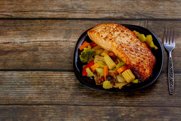 Tasty fried pink salmon with asian vegetables on plate with fork.