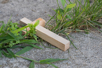 Wooden Cross on a Sidewalk with Grass Growing Around It