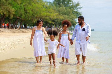 Happy African american family holding hands and walking together on the beach during holiday.