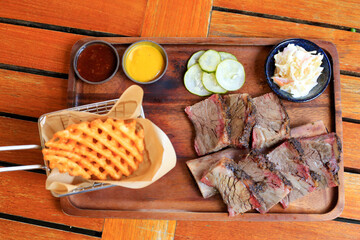 Beef steak with mustard sauce and cucumber and pickles and basket of french fries placed on a wooden tray close up.