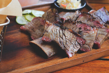 Beef steak with mustard sauce and cucumber and pickles and basket of french fries placed on a wooden tray close up.