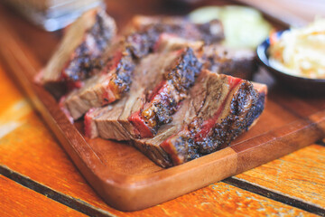 Beef steak with mustard sauce and cucumber and pickles and basket of french fries placed on a wooden tray close up.