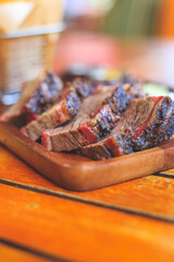Beef steak with mustard sauce and cucumber and pickles and basket of french fries placed on a wooden tray close up.