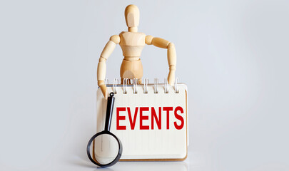 Wooden man shows with a hand to white notepad with text EVENTS